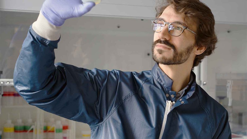 man in a blue plastic lab coat holding up a sample cup