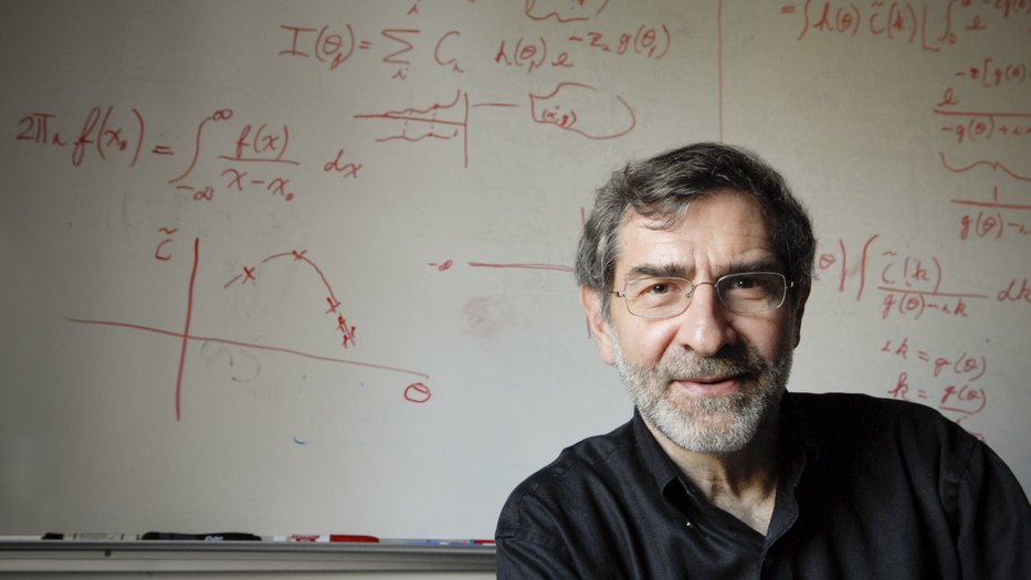 Henry Lester, Caltech's Bren Professor of Biology and Biological Engineering, seated in front of a whiteboard covered in complex mathematical equations written in red marker.