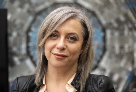 Headshot of woman with short gray hair in front of a picture of scientific equipment