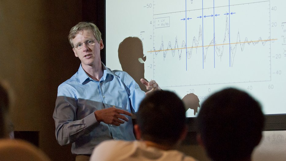 Professor Schneider teaching in front of a classroom with a graph behind him