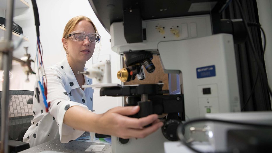 Woman in safetly goggles adjusting a microscope