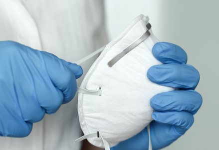 blue-gloved hands holding N95 mask