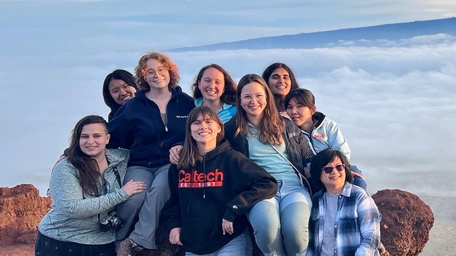 Caltech students stand together at the top of a mountain with an expansive valley view in the background.