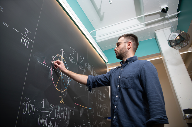 Alexander Dunn working on a physics equation on a chalk board.