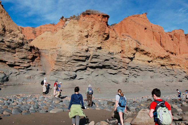 Geology students walking towards a tall red rock feature.